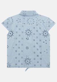 Light blue cotton shirt with short sleeves, featuring floral embroidery and cut-out patterns, collared with a tied hem detail at the back.