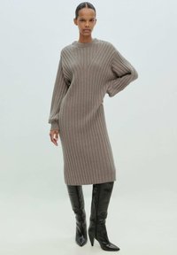 Grau geripptes Strickkleid mit langen Ärmeln, das einen runden Ausschnitt und strukturierte vertikale Streifen aufweist. Kombiniert mit schwarzen kniehohen Stiefeln mit spitzer Zehe.