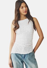 Blusa senza maniche bianca con una texture a raccolto, caratterizzata da un collo rotondo e una silhouette fluida, abbinata a jeans in denim azzurro chiaro.