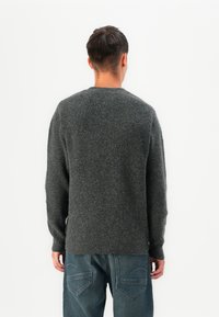 Dark gray knitted sweater with long sleeves, a round neckline, and a relaxed fit, paired with blue jeans. Textured fabric with visible stitching.