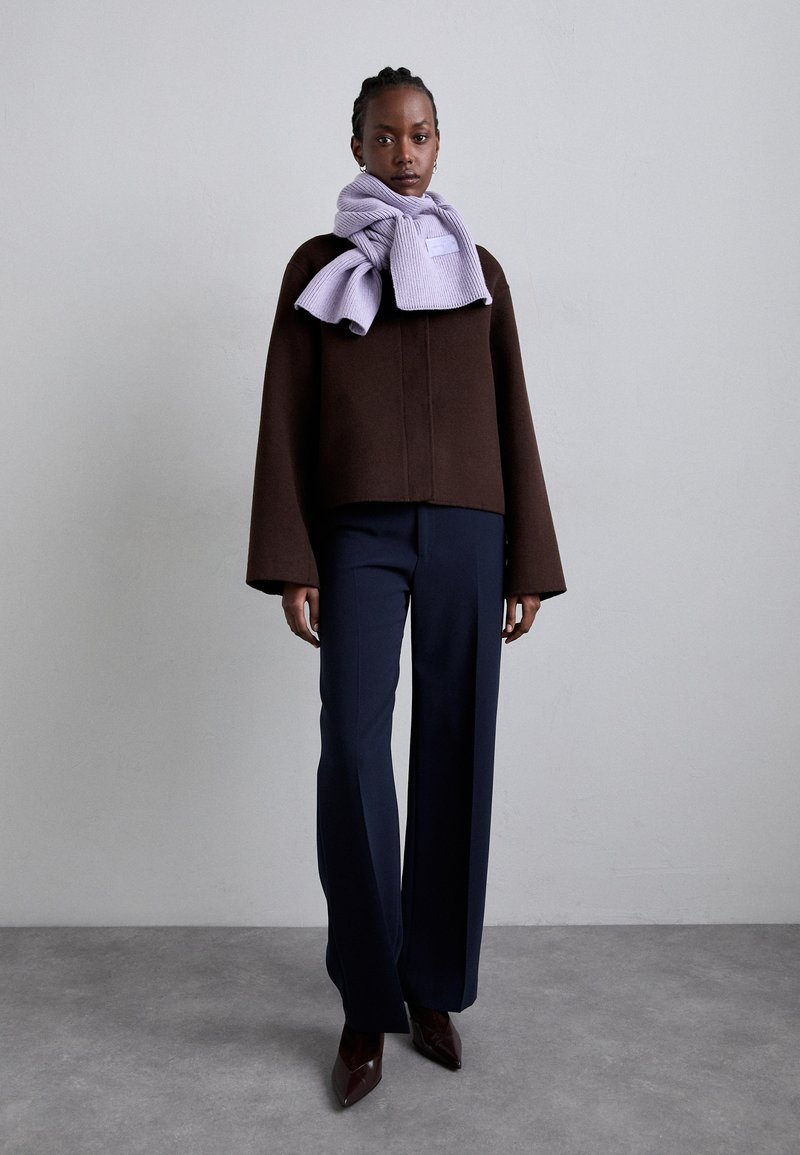 Brązowa krótka kurtka z szerokimi rękawami, zestawiona z granatowymi spodniami w szerokim kroju i jasnofioletowym prążkowanym szalem. Brązowe czółenka z wąskim noskiem.