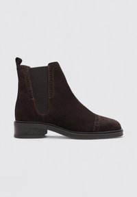 Bottine en suède marron foncé avec des panneaux élastiques sur les côtés, des détails brogue et un petit talon carré. Dispose d'une languette à l'arrière pour un enfilage facile.