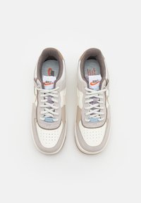 Paire de baskets Nike blanches et beiges avec doublure grise et lacets blancs vues de dessus sur un fond uni.