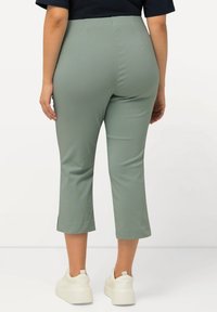Pantalons courts extensibles vert clair à taille haute avec des fentes sur les côtés, portés avec des baskets blanches à plateforme.