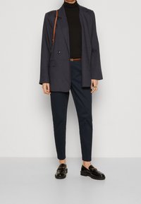 Navy blazer with a structured design, black turtleneck, tailored navy pants, and black loafers with gold hardware accents.