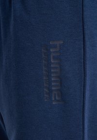 Vêtements de sport en tissu navy, présentant une texture lisse et un logo en relief bien visible portant l'inscription "hummel SPORTSWEAR" disposé en vertical.