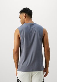 Maglietta senza maniche grigia con scollatura rotonda e texture di tessuto liscia, con una vestibilità rilassata e dettagli sottili nella cucitura posteriore.