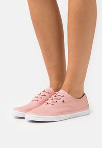 Roze platnene tenisice s bijelim gumenim potplatima i vezicama, s malim plavim, crvenim i bijelim logotipom sa strane.