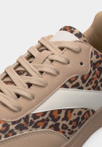 Αθλητικό παπούτσι με μπεζ κορδόνια και πάνελ από σουέντ, διακοσμημένο με ύφασμα με σχέδιο λεοπάρ και λευκή ρίγα στο πλάι.