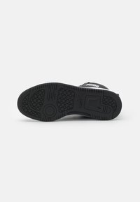 Semelle de sneaker Puma noire avec motifs de bande de roulement hexagonaux et éléments de grip circulaires, vue par le dessous sur un fond uni.