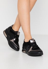 Sneaker sportive nere con tomaia in mesh, accenti in suede, dettagli metallici e lacci neri. La suola presenta un accento metallico nel tallone.