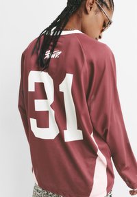 Bordo mrežasti dugi rukav jersey s belim "31" i logotipom na leđima. Ima ružičaste bočne naglaske, prikazuje udoban kroj i prozračnu teksturu.