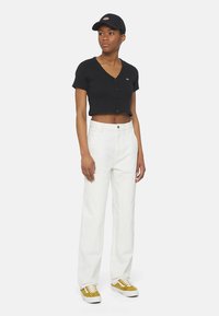 Svart kortärmad knapplöst topp, vita högmidjade byxor, gula och vita sneakers, och en svart keps. Minimalistisk och avslappnad outfit.