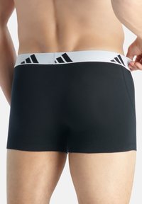 Svarta boxerkalsonger med en vit elastisk midjeband som har svarta ränder. Slät tyg, figurnära design och midjlång längd.