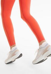 Felle oranje legging met een gladde textuur en contrasterende stiksels, gecombineerd met lichte sneakers met gaasdetails en een gevoerde zool.