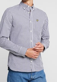 Camicia button-down caratterizzata da un motivo a quadretti navy e bianchi, maniche lunghe e una tasca sul petto con un piccolo logo giallo. Materiale in cotone.