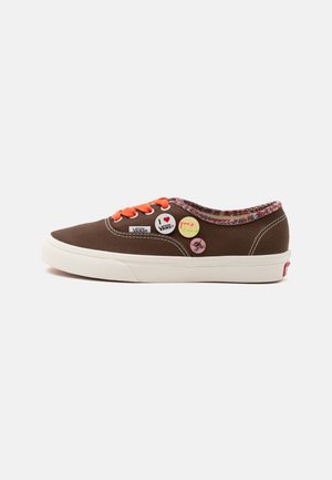 Baskets Vans marron avec semelle blanche, lacets orange, doublure à motifs colorés et pins décoratifs avec différents motifs et logos sur le côté.