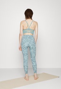 Top desportivo azul claro, cropped, com um design de costas cruzadas e leggins a condizer com um padrão botânico branco. Textura suave e forma ajustada.