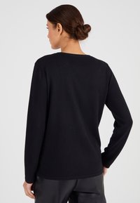 Suéter negro de manga larga con cuello redondo. Fabricado en material suave, presenta un corte relajado y un diseño minimalista sin adornos.