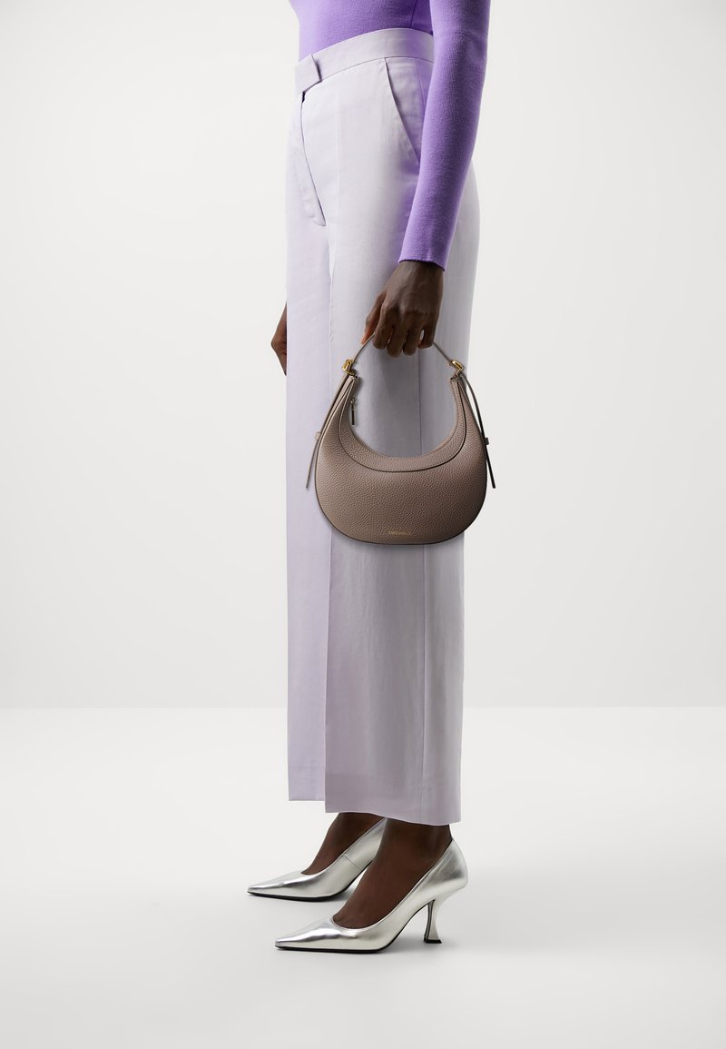 Borsa a tracolla in stile hobo in pelle grigio chiaro con texture a pelle di pesca e hardware dorato; tenuta in mano. Abbinata a pantaloni lavanda e décolleté argentati a punta.