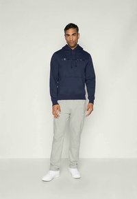 Felpa navy con logo sul petto, abbinata a pantaloni della tuta grigi chiari. Il modello indossa sneakers bianche. Design semplice e materiali morbidi.
