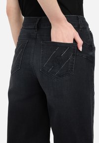 I jeans in denim neri presentano una vita alta, un design a cinque tasche, con una particolare cucitura decorata sulle tasche posteriori.