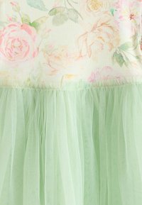 Corsage à motif floral avec des roses rose pastel et vertes au-dessus d'une jupe en tulle vert clair froncée sur une robe.