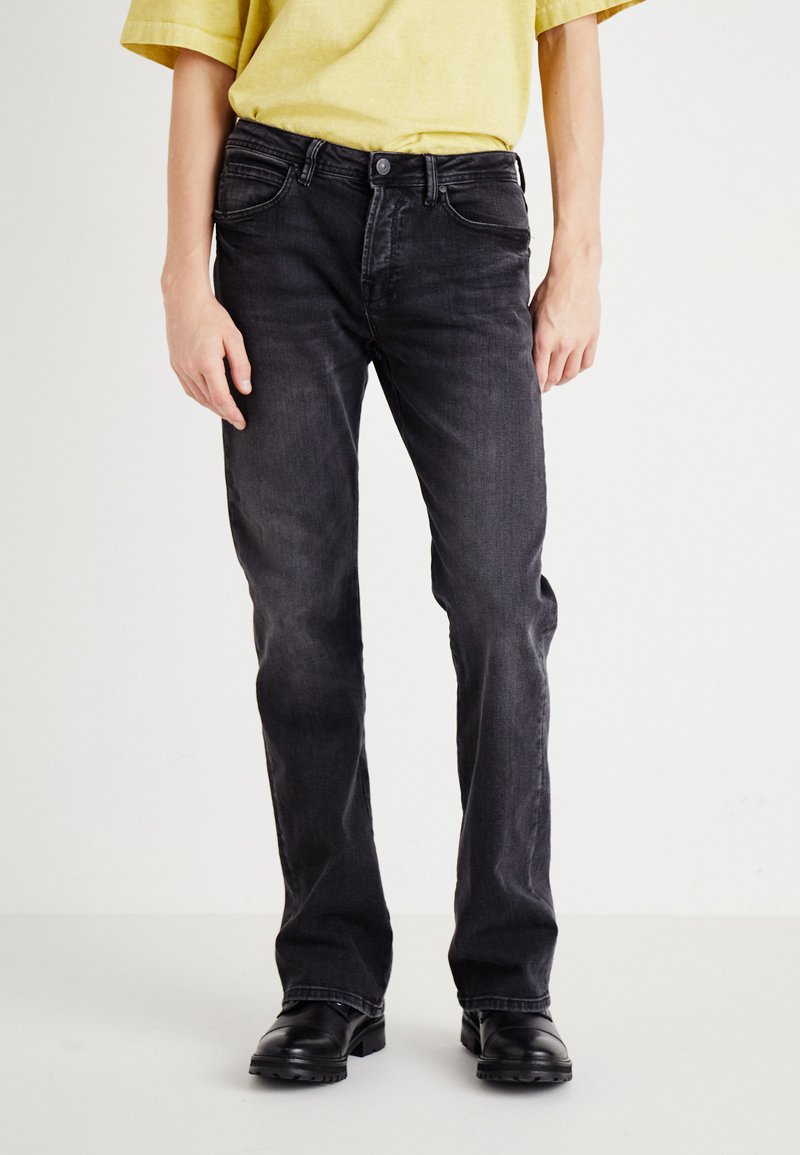 Črne denim hlače s ravnim krojem, ki imajo vidne žepke in rahlo zbledelost. Zesafte s lahkim rumenim srajcem in črnimi čevlji.