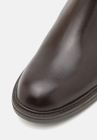 Hnědé kožené kotníkové boty s oválnou špičkou, hladkým povrchem a dekorativním prošíváním podél podešve. Klasický design s lesklým povrchem.