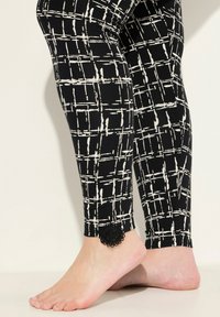 Leggings noirs avec un motif de quadrillage blanc. Présentent un accent décoratif en dentelle noire près de la cheville. Tissu doux et design ajusté.