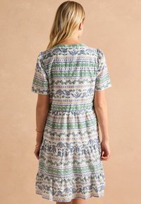 Kvetinové šaty s striedajúcimi sa modrými a zelenými vzormi na bielom pozadí; krátke rukávy, vrstvený riasený spodok a okrúhly výstrih.