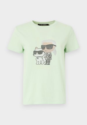 T-shirt en coton vert clair avec un design de personnage et de chat, tous deux portant des lunettes de soleil avec des détails en points. Col rond et manches courtes.