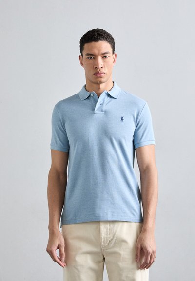 Polo bleu clair en coton, présentant une texture douce, des manches courtes, un col et un petit logo sombre sur la poitrine gauche.