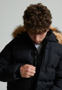Black puffer jacket with a fur-lined hood, featuring a zip closure and visible stitching, focusing on warmth and insulation.