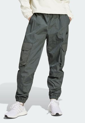 Mørkegrå cargobukser med elastiske manchetter, båret med hvide sneakers og en lyse farvet langærmet top, hænderne i lommerne.