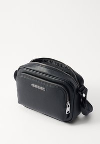 Schwarze Leder-Umhängetasche mit zwei Reißverschlussfächern, strukturierter Oberfläche und silberner Hardware. Mit einem geprägten Logo auf der Vorderseite.