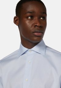 Ljusblå skjorta med knäppning och en strukturerad krage samt en mjuk yta. Har vita knappar och en figurnära passform.