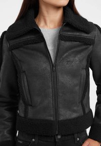 Giubbotto in shearling nero con colletto strutturato, chiusura a zip e finitura testurizzata. Presenta un rivestimento morbido a contrasto lungo il colletto e l'orlo.