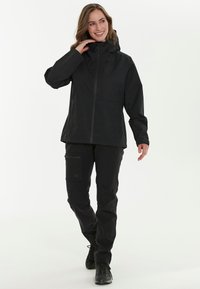 Sort vandtæt jakke med lynlås og justerbar hætte, parret med sorte bukser med en sidelomme og et strømlinet design.