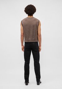 Suéter sin mangas marrón con un tejido texturizado y un diseño corto. Combinado con jeans negros ajustados y calzado negro. Vista trasera visible.