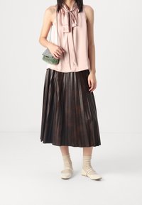 Blusa di satin rosa chiaro con colletto annodato, gonna di pelle marrone scuro plissettata, calze beige e ballerine color avorio. Piccola borsa verde a fantasia.
