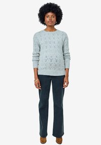 Hellblauer Strickpullover mit strukturiertem Muster und seitlichen Knopfakzenten, kombiniert mit dunkelblauen Schlagjeans und braunen Stiefeletten.