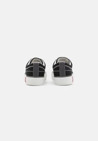 Adidași negri din pânză, cu tălpi de cauciuc alb, tocuri gri și accente roșii. Prezintă cusături contrastante și un design de profil scăzut.