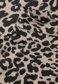 Beżowy materiał z czarnym wzorem w panterę. Tekstura wydaje się prążkowana, co dodaje głębi i interesu do projektu.