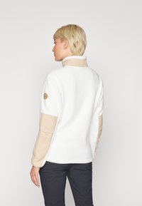 Pullover in pile bianco conAccenti beige e colletto alto. Presenta un materiale testurizzato e un logo rotondo sulla manica sinistra.