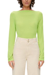 Lange mouwen top van helder limoengroen stof met een bootnek, gedragen met beige high-waisted broek met een sluiting met twee knopen.