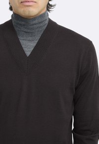 Maglione nero a scollo a V indossato sopra un dolcevita grigio. Il maglione presenta bordi a coste e una texture liscia. Lo stile aderente mette in risalto la silhouette.