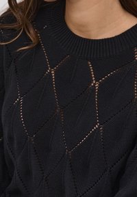Schwarzer Strickpullover mit einem strukturierten Muster aus Rautenshapes und offenen Nähten. Gerippter Halsausschnitt und detaillierte blattähnliche Designs.