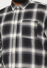 Karierte Hemdjacke in Schwarz und Weiß, mit einer Brusttasche, strukturiertem Kragen und strapazierfähigem Stoff mit kontrastierenden Linien und Mustern.