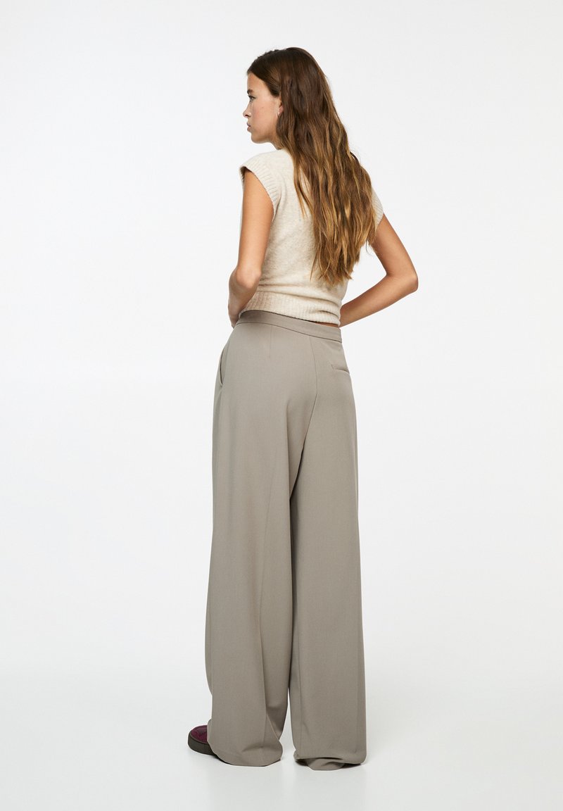 Haut beige ajusté associé à un pantalon ample gris clair avec une texture lisse et des poches latérales. L'ensemble a un design décontracté.